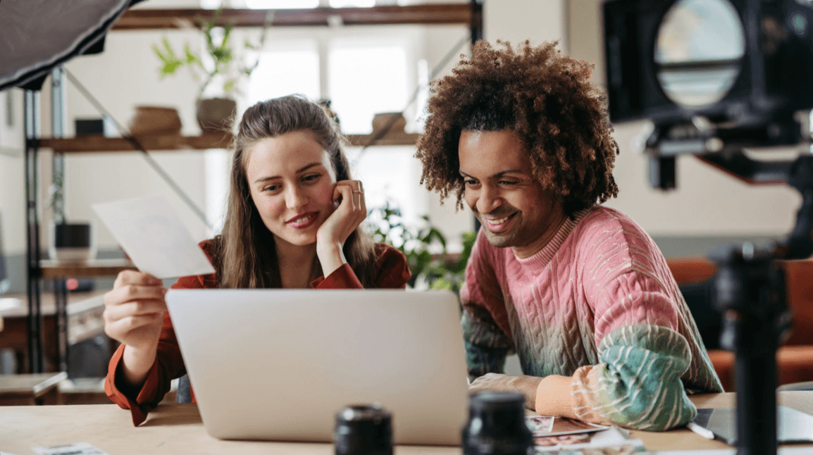 Two people smiling as they look at a laptop together at a table